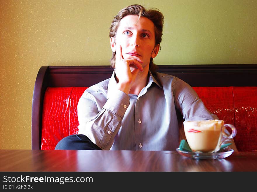 Cup of coffee and young man in modern cafe interior