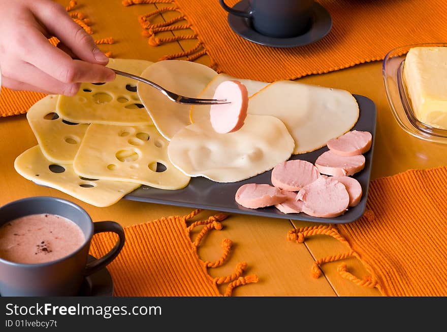 A hand is holding a piece of sausages at the breakfast table. A hand is holding a piece of sausages at the breakfast table