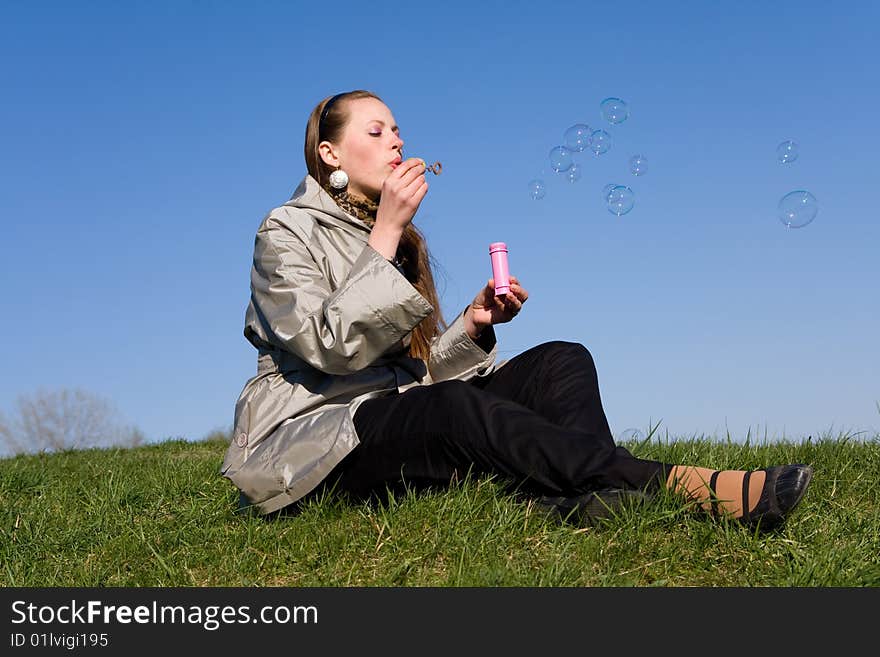 Beautiful girl makes soap bubble on a grass