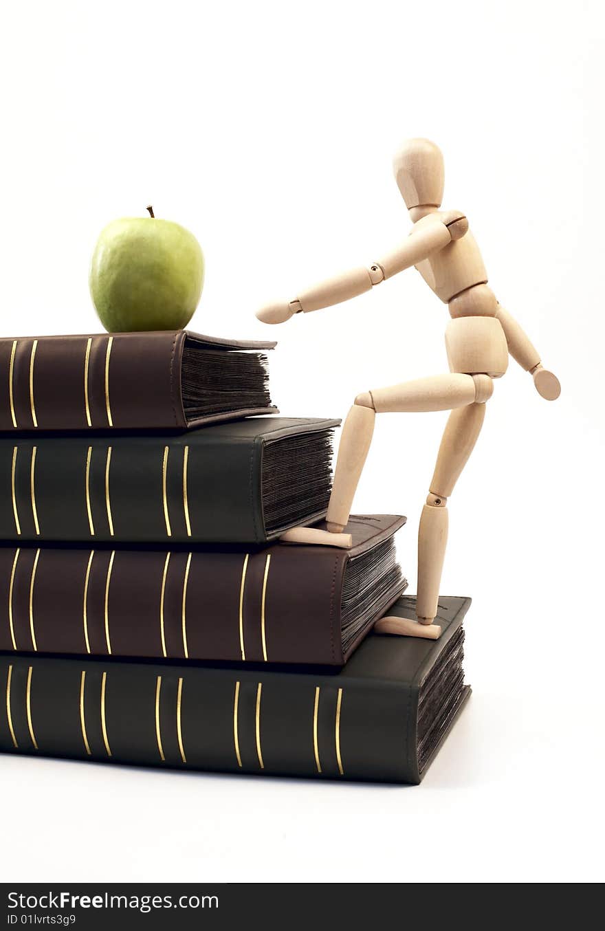 Wooden figure on a stack of books going up for an apple