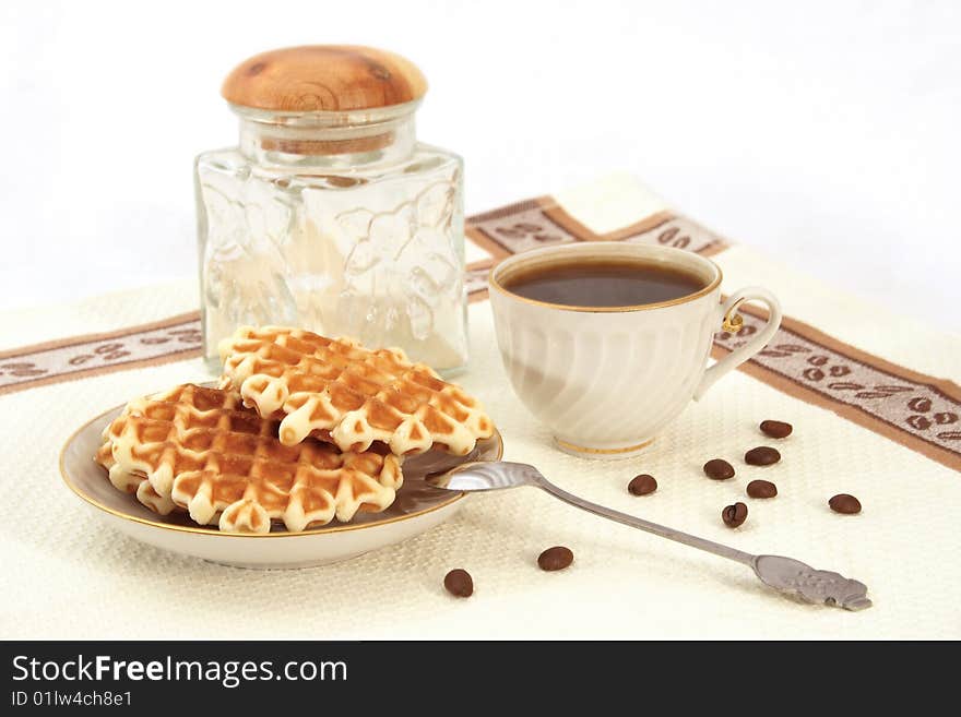 Wafers on a saucer, a porcelain cup from coffee, glass jar, grains, a teaspoon on a napkin. Wafers on a saucer, a porcelain cup from coffee, glass jar, grains, a teaspoon on a napkin