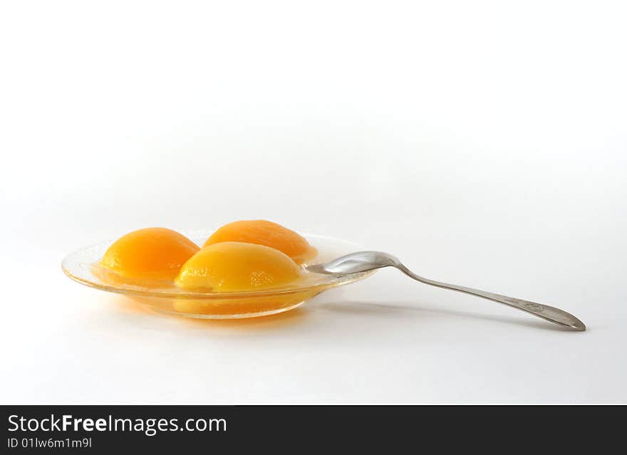 Segments of tinned peaches on a glass saucer with a dessertspoon on a white background. Segments of tinned peaches on a glass saucer with a dessertspoon on a white background