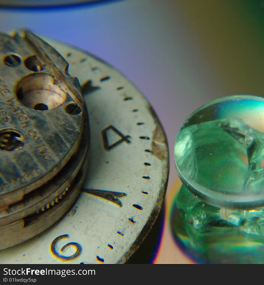 Three parts of old watches are placed on a cd and a piece of broken glass showcasing the intricate workings of an almost lost craftsmanship.  A crystal sits next to a large watchface with the workings sitting on top. Three parts of old watches are placed on a cd and a piece of broken glass showcasing the intricate workings of an almost lost craftsmanship.  A crystal sits next to a large watchface with the workings sitting on top.