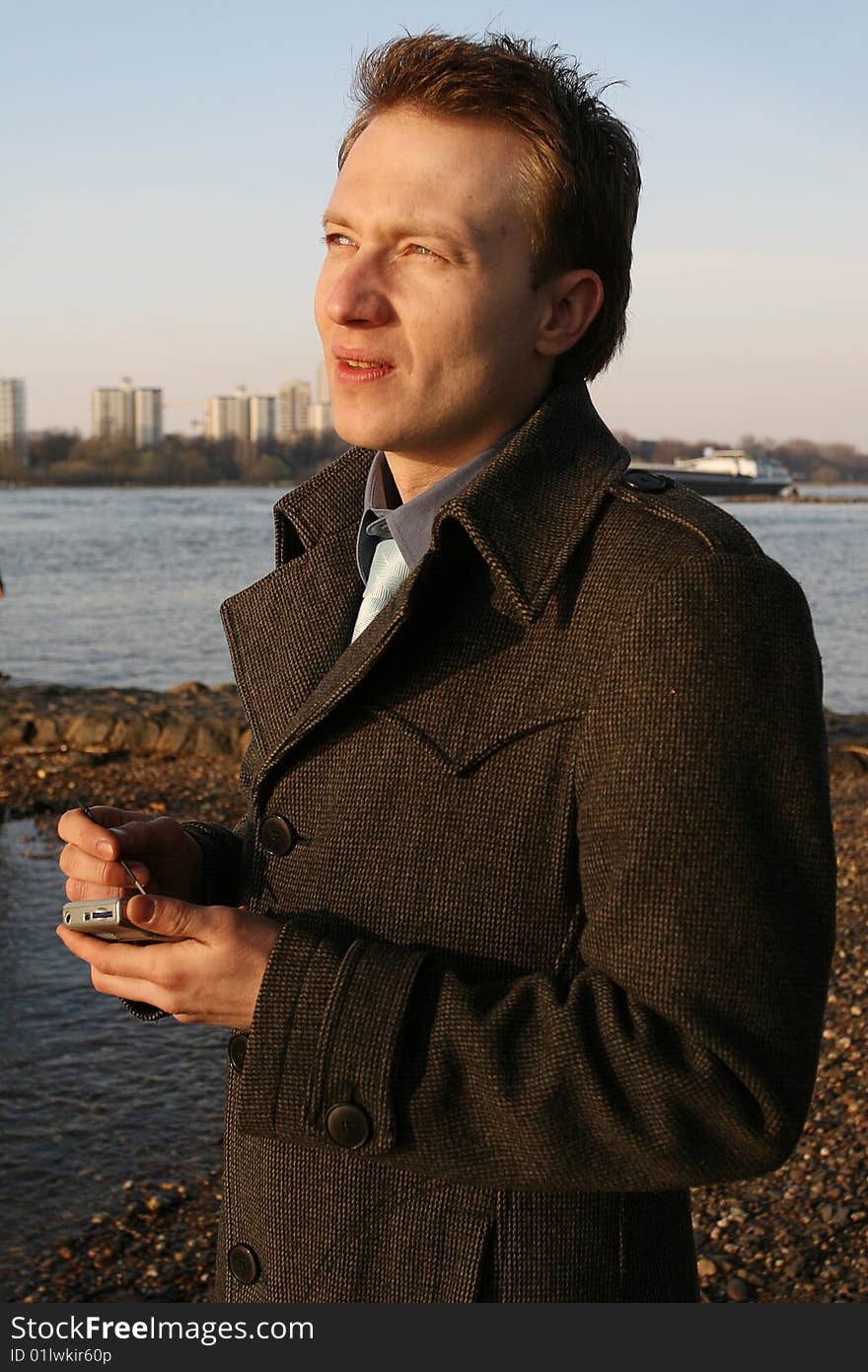 Businessman typing on a pager standing by the river. Businessman typing on a pager standing by the river