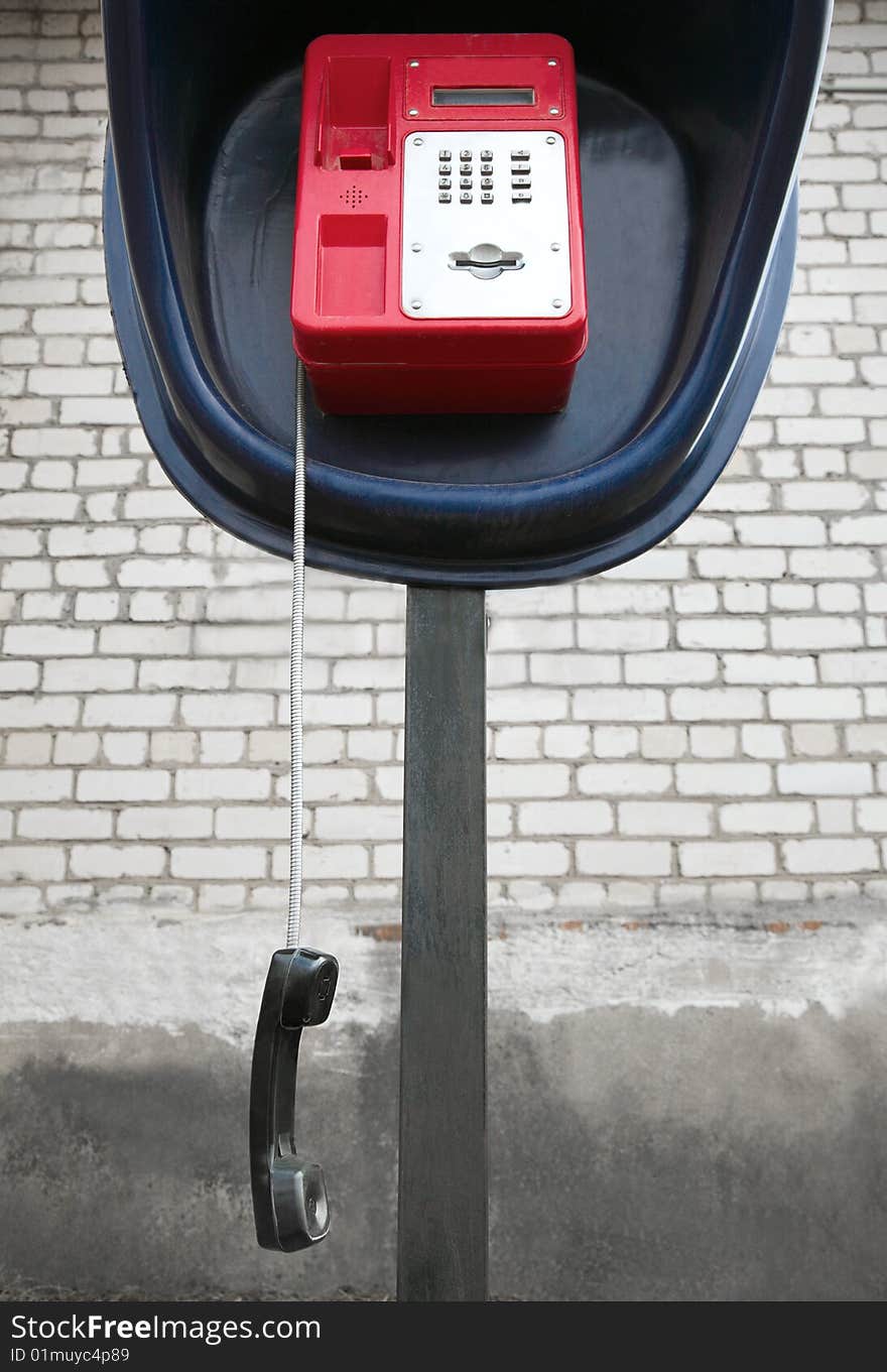 The red payphone with a hanging tube. The red payphone with a hanging tube