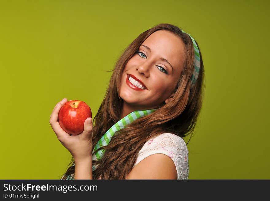 Brunette holding apple and smiling against a green background