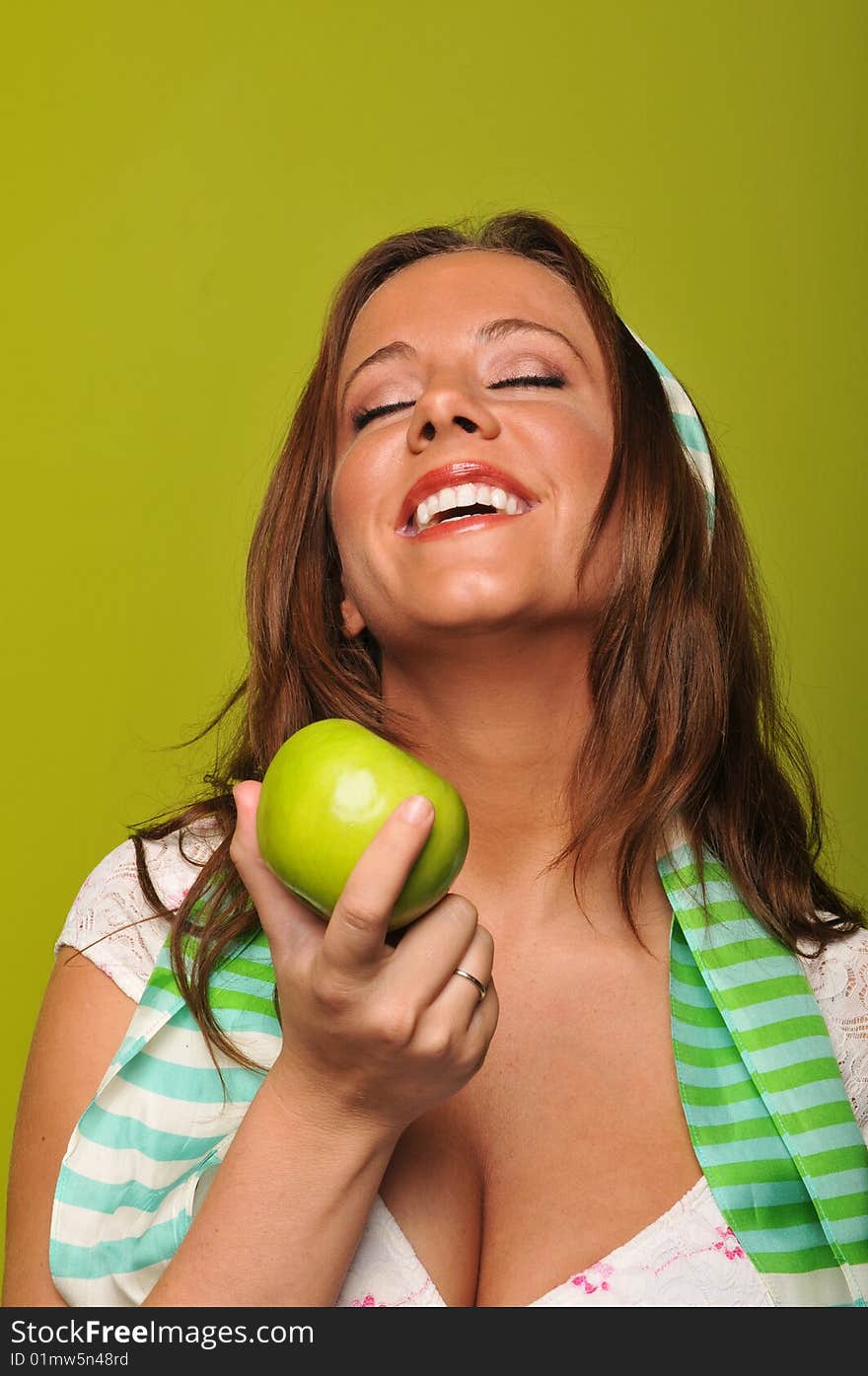 Brunette holding apple and smiling against a green background