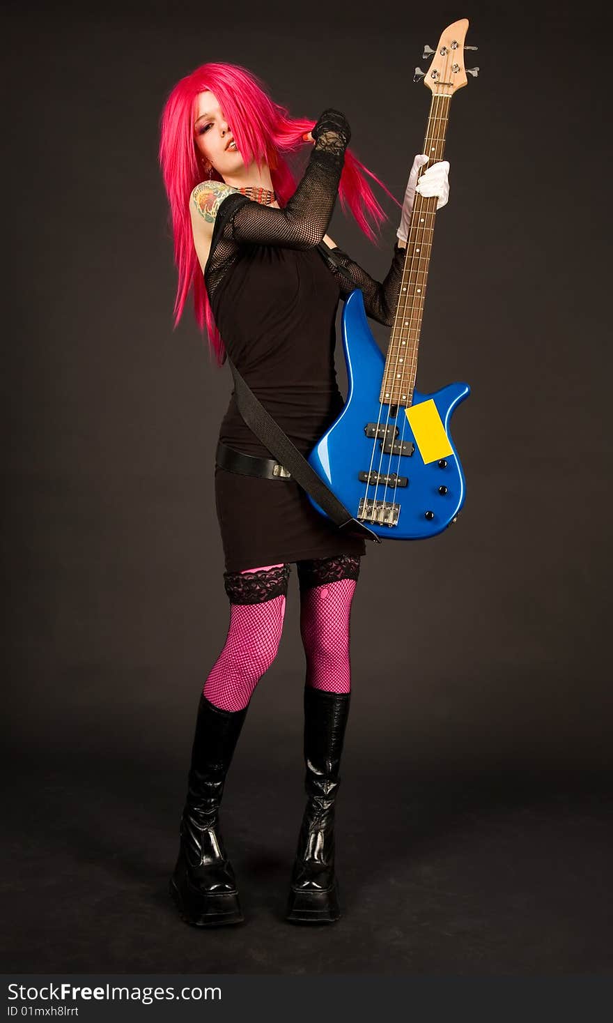 Attractive girl putting on bass guitar, studio shot on black background