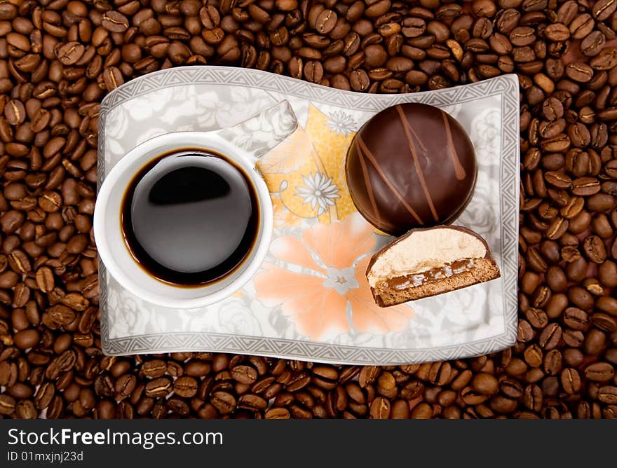 Coffee cup with sweets on beans background, high angle view