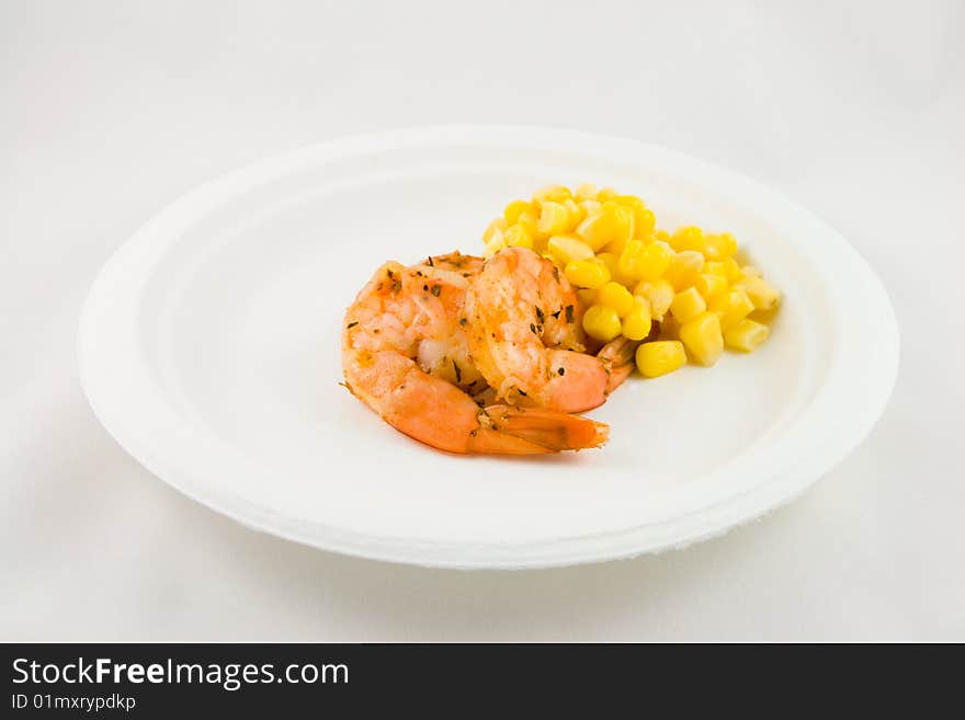 Spicy king prawns with yellow sweetcorn on a white plate on a white background. Spicy king prawns with yellow sweetcorn on a white plate on a white background