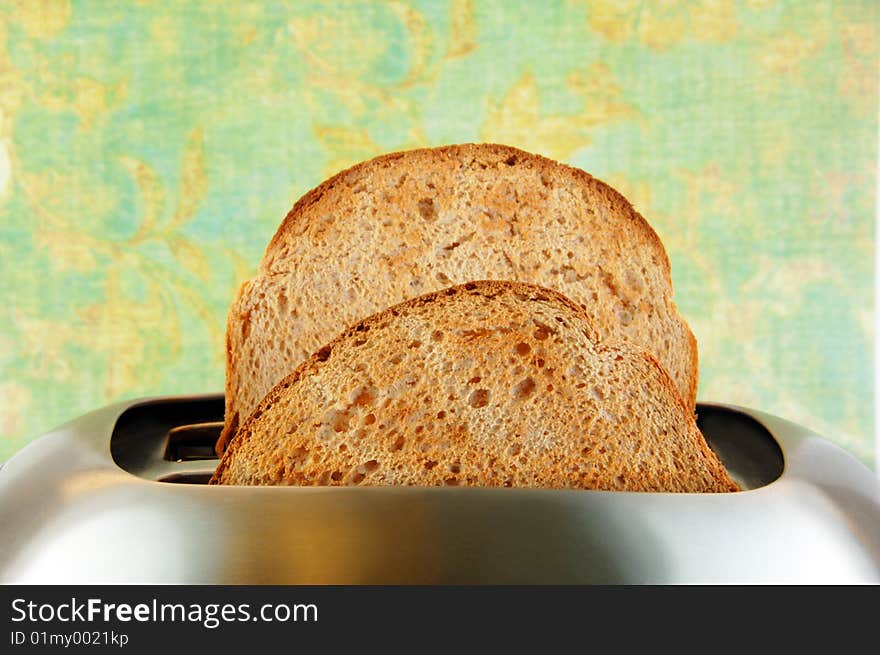 Toasted bread in a stainless steel toaster with a green background. Toasted bread in a stainless steel toaster with a green background.