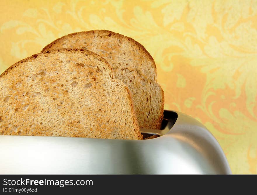 Toasted bread in a stainless steel toaster with a yellow background. Toasted bread in a stainless steel toaster with a yellow background.