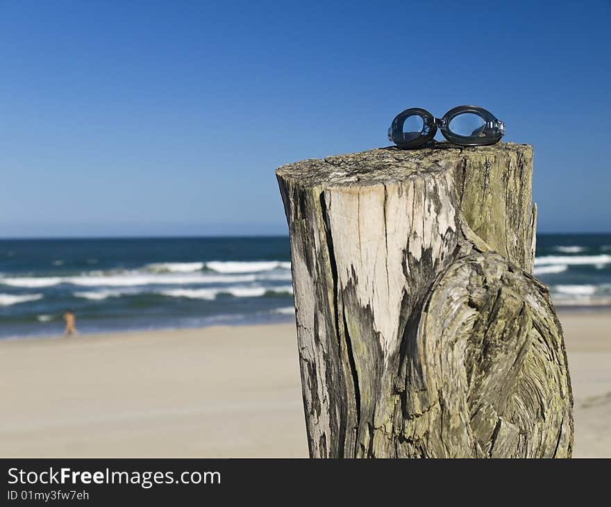 A pair of goggles sitting over a log in the beach.