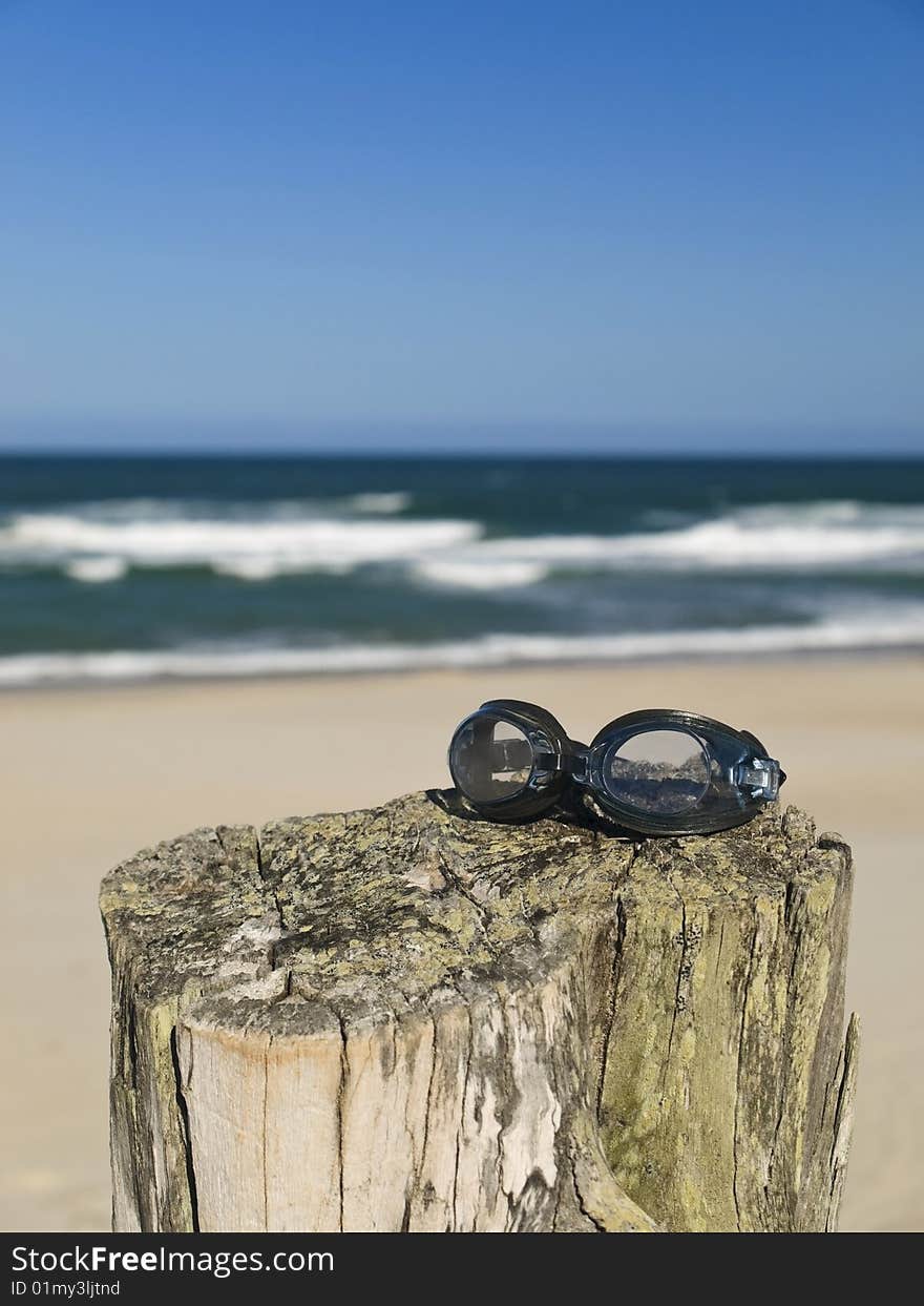 A pair of goggles sitting over a log in the beach.