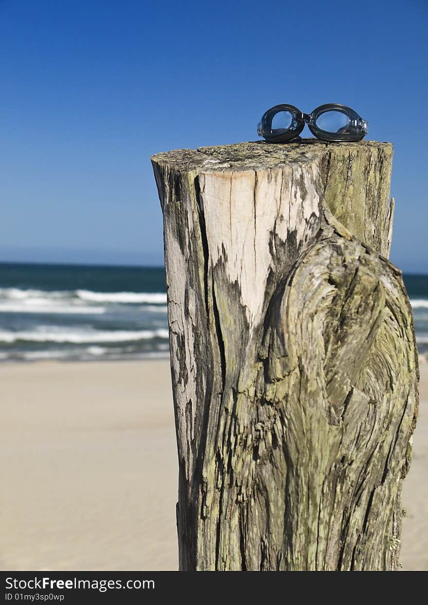 A pair of goggles sitting over a log in the beach.