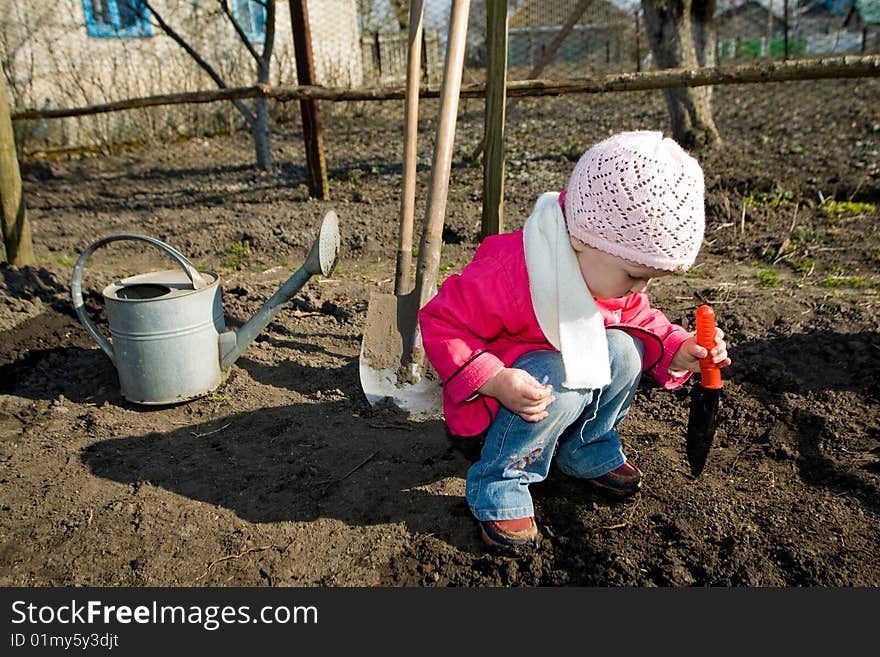 A pretty little girl squatting down on the ground in her grandfather's kitchen garden. A pretty little girl squatting down on the ground in her grandfather's kitchen garden