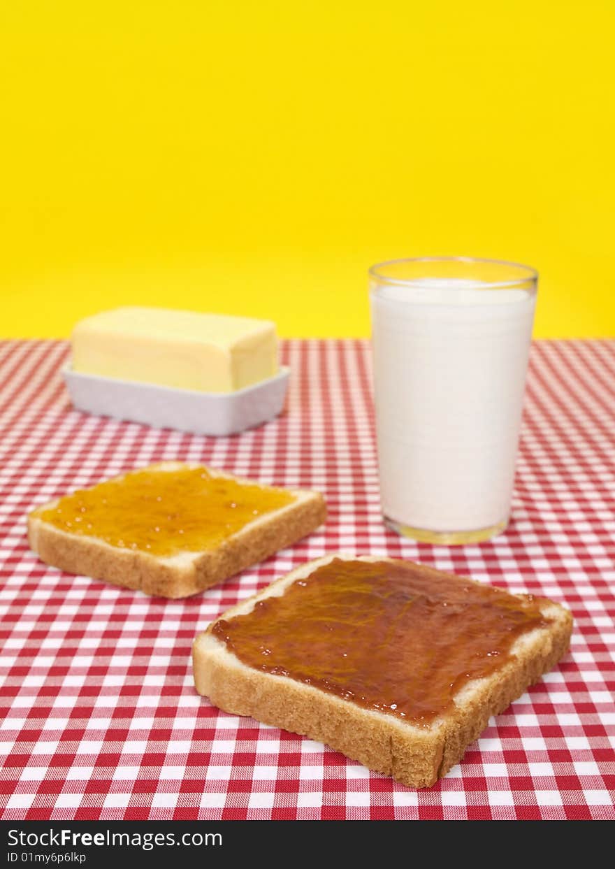 Two slices of bread spread with jam, a glass of milk and a butter stick. Two slices of bread spread with jam, a glass of milk and a butter stick.