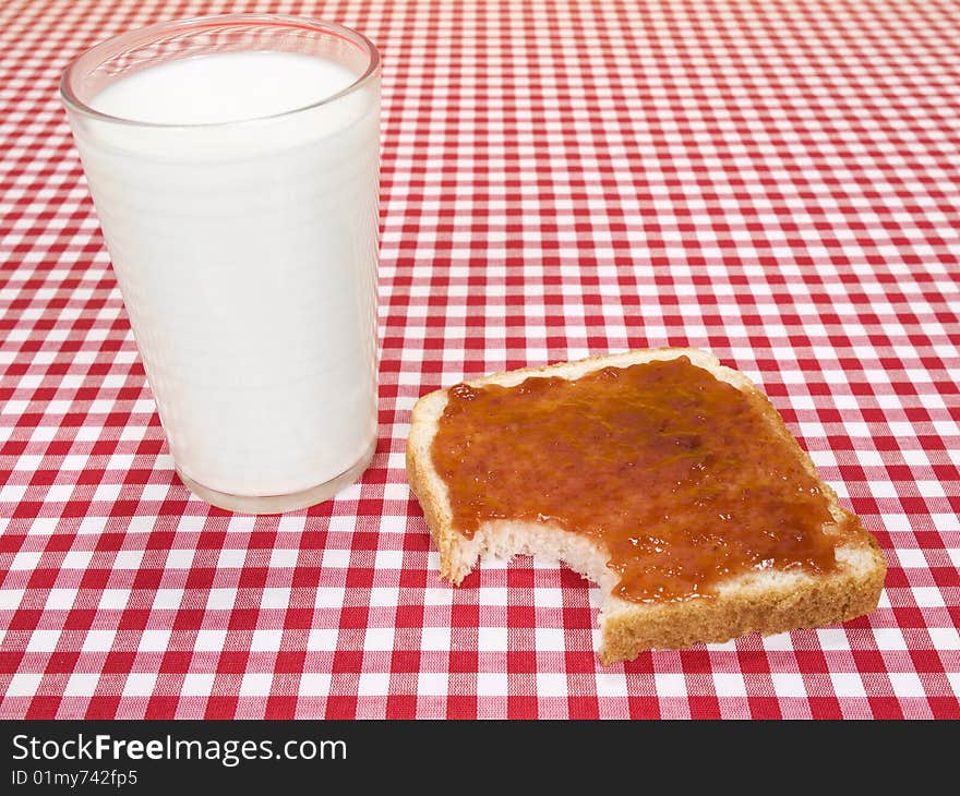 A glass of milk and a toast spread with jam, with a bite missing. A glass of milk and a toast spread with jam, with a bite missing.