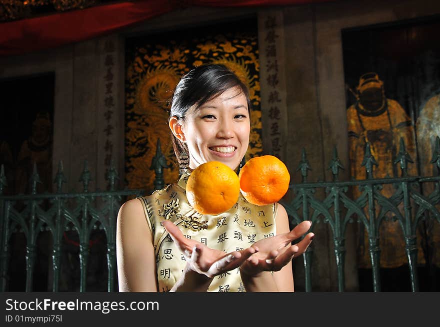 Beautiful Asian woman in cheongsam holding two oranges, suitable for Chinese New Year occasion. Beautiful Asian woman in cheongsam holding two oranges, suitable for Chinese New Year occasion.