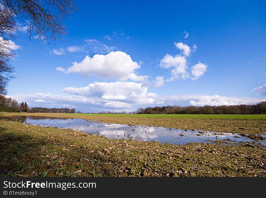 Farmland after the rain with puddle and blue sky and some clouds