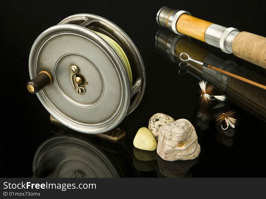 Still life of old fly reel with some flies with a bamboo rod and stones