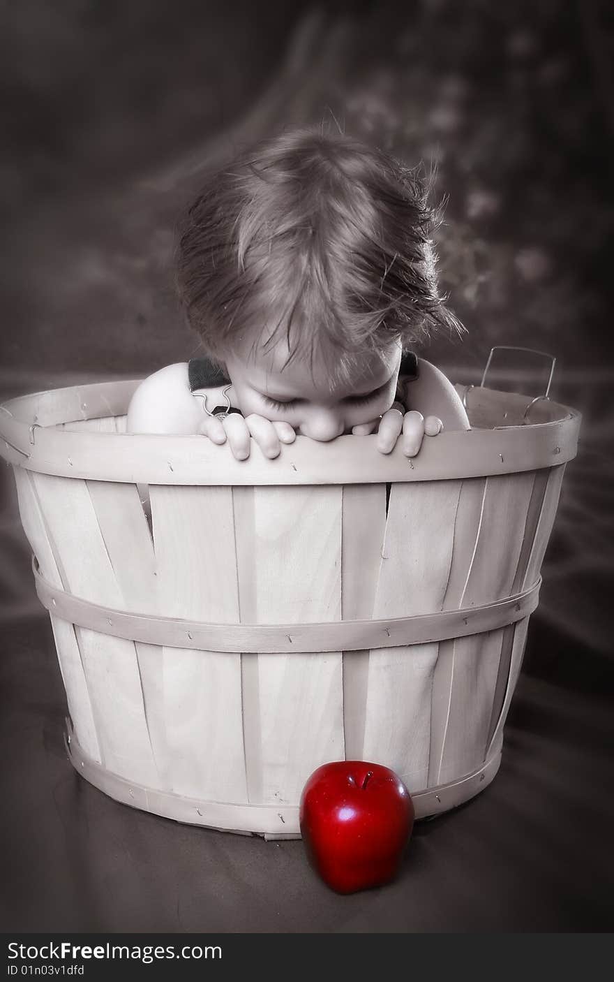 Boy sitting in Apple Basket looking down at bright red apple