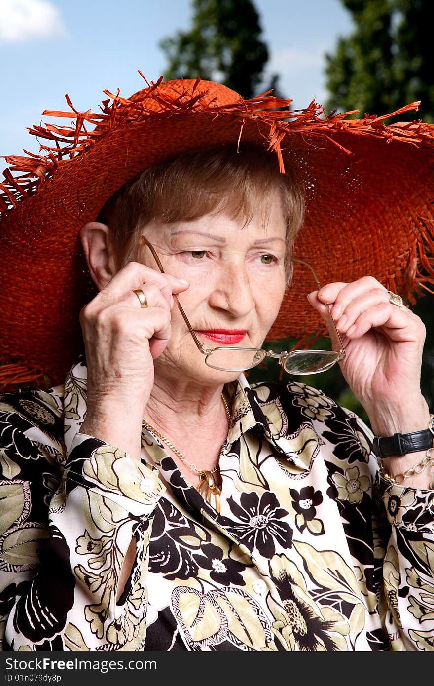 Adorable elderly woman wearing straw hat and putting on her glasses. Adorable elderly woman wearing straw hat and putting on her glasses.