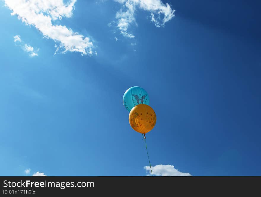 Two balloons shined with the sun through clouds against the sky