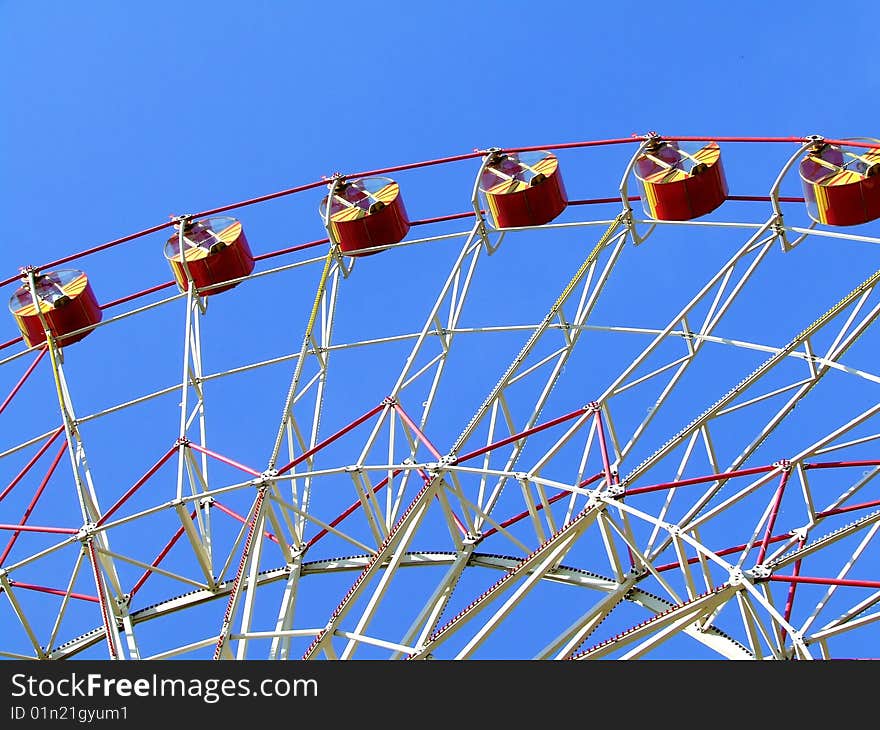 Big Ferris wheel with colored cabins on cloudy sky