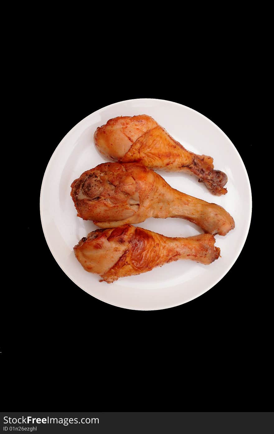 Three roasted chicken legs on the plate over black. Three roasted chicken legs on the plate over black.