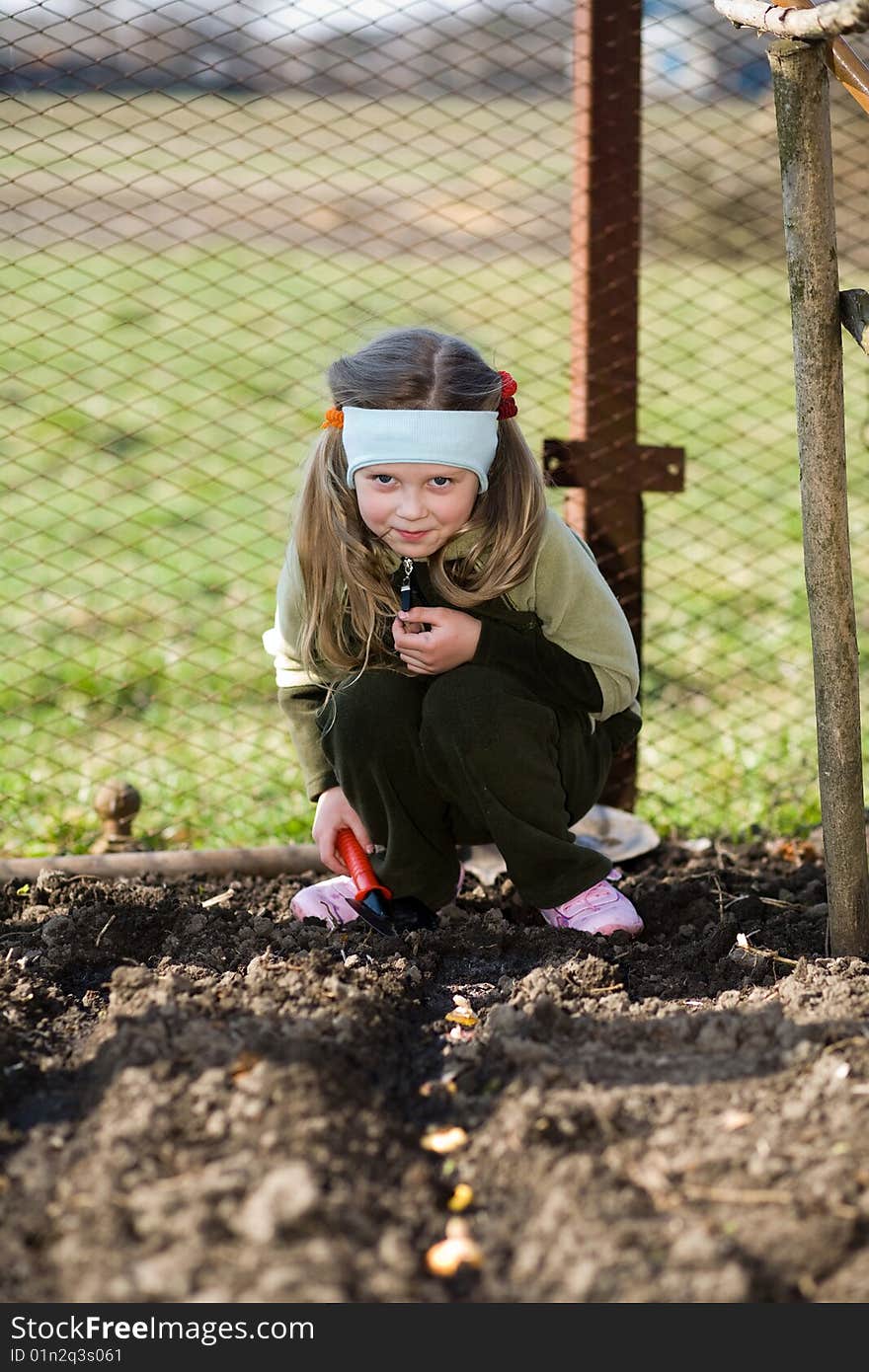 A pretty little girl squatting down on the ground in her grandfather's kitchen garden. A pretty little girl squatting down on the ground in her grandfather's kitchen garden