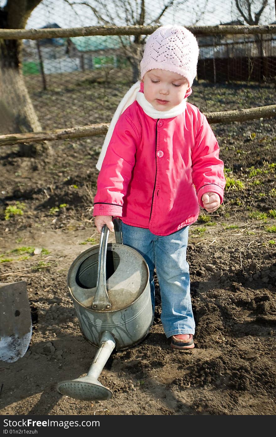 A pretty little girl watering soil  with a watering can in  her grandfather's  kitchen garden. A pretty little girl watering soil  with a watering can in  her grandfather's  kitchen garden