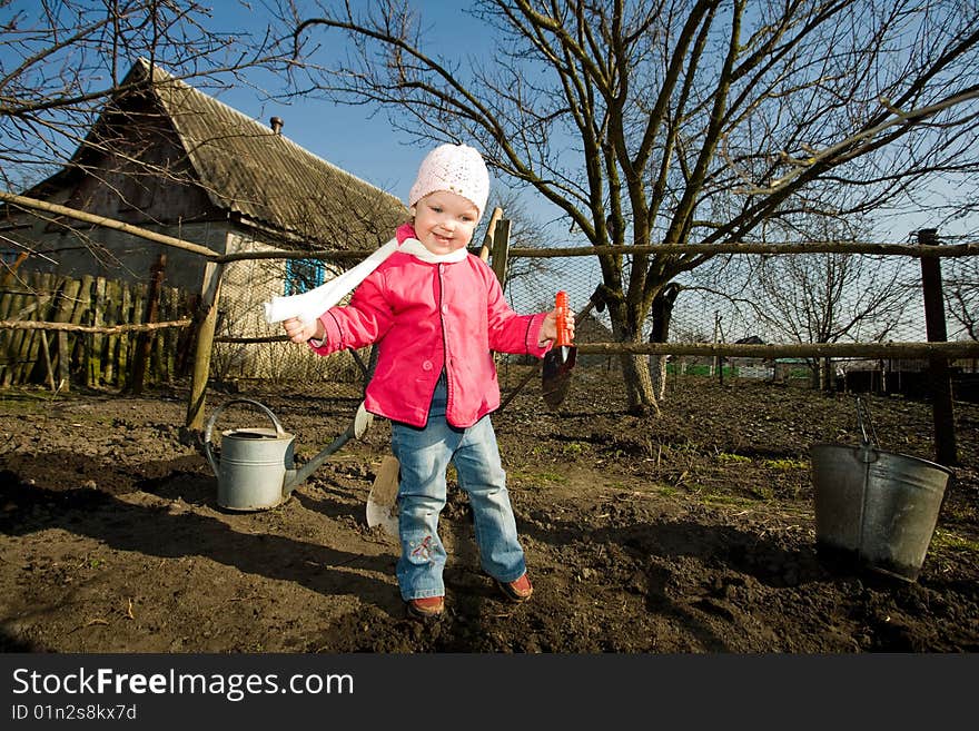 A smiling pretty little girl with a toy spade in hand in her grandfather's kitchen garden. A smiling pretty little girl with a toy spade in hand in her grandfather's kitchen garden