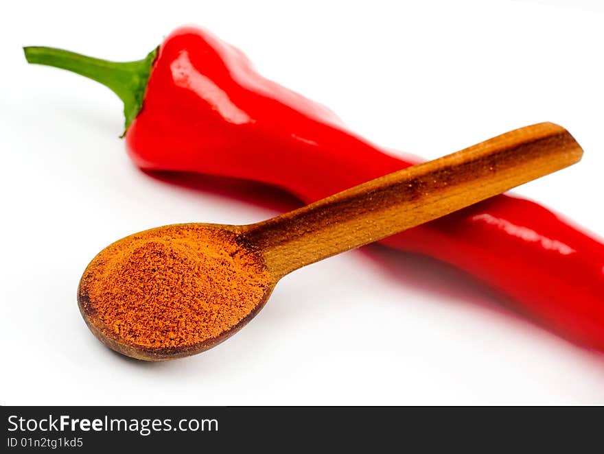 A composition of a wooden spoonful across a cut pod of red hot pepper on a white background. A composition of a wooden spoonful across a cut pod of red hot pepper on a white background