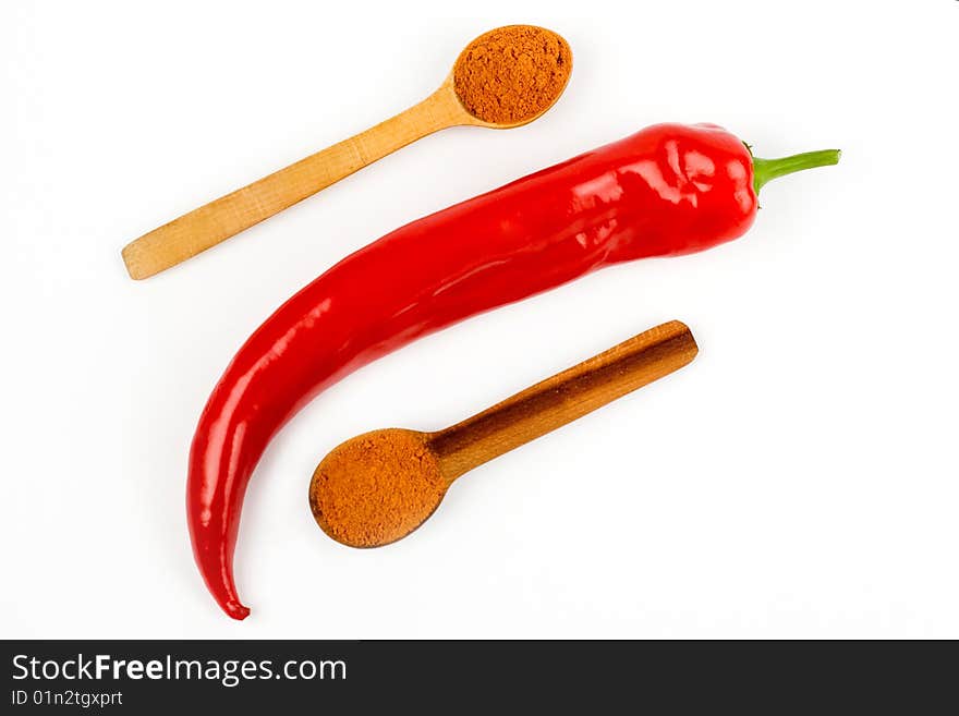 A composition of a pod of red chile pepper  and two wooden spoonful of red ground pepper on a white background. A composition of a pod of red chile pepper  and two wooden spoonful of red ground pepper on a white background