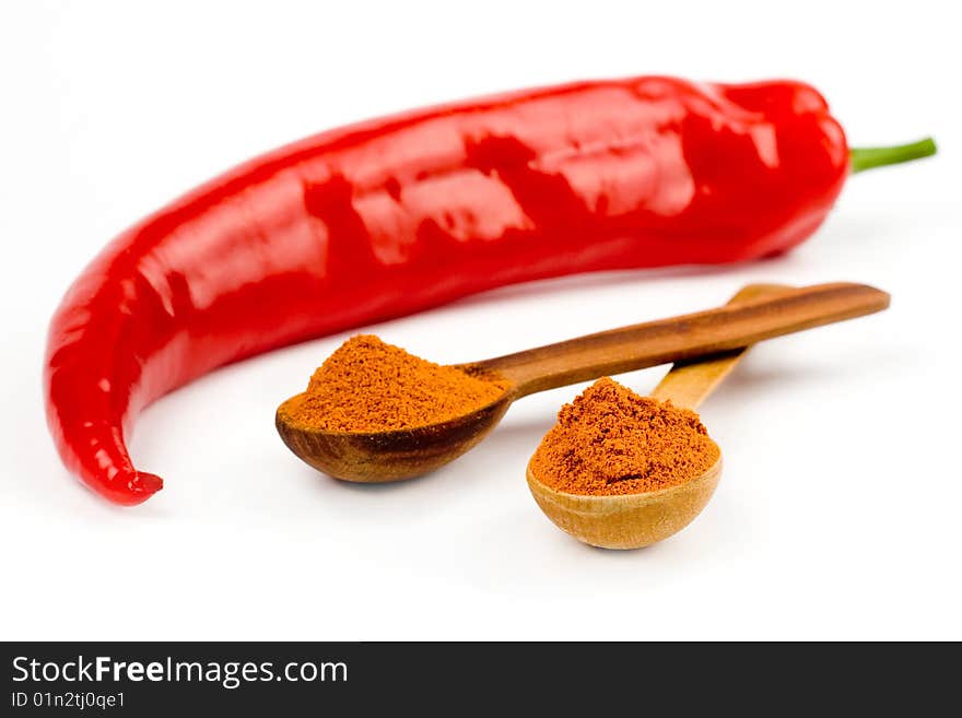 A composition of two intersected wooden spoonfull and a pod of red hot pepper on a white background. A composition of two intersected wooden spoonfull and a pod of red hot pepper on a white background