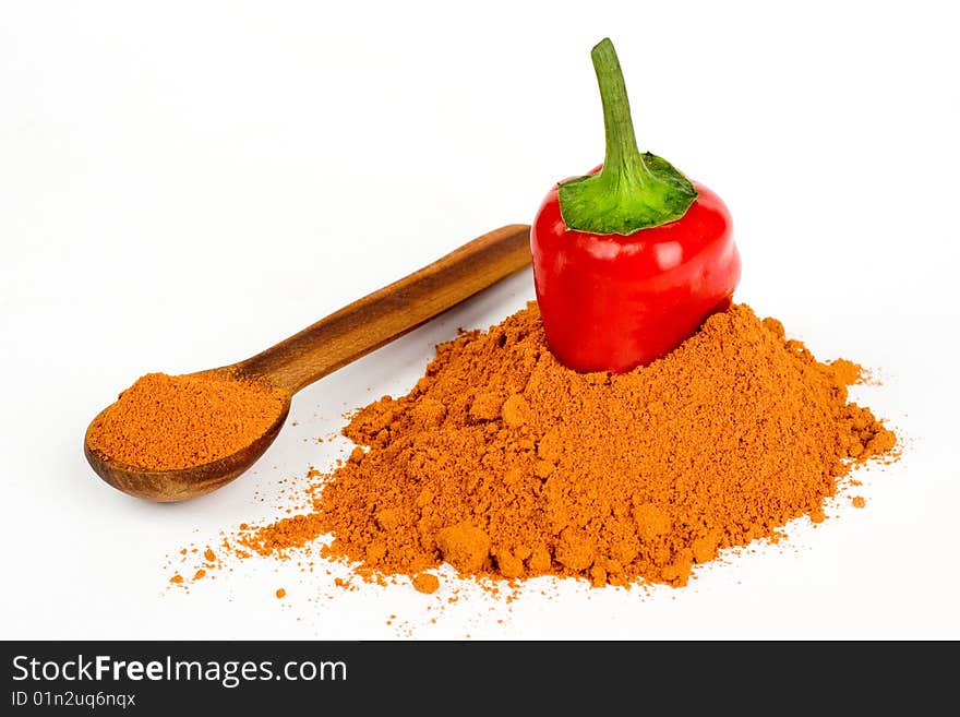 A cut pod of red hot pepper in ground pepper and a wooden spoonful of ground pepper on a white background. A cut pod of red hot pepper in ground pepper and a wooden spoonful of ground pepper on a white background