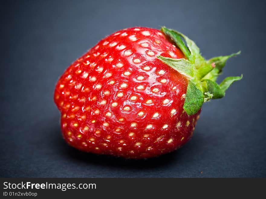 A signle strawberry fruit isolated on a plain dark background