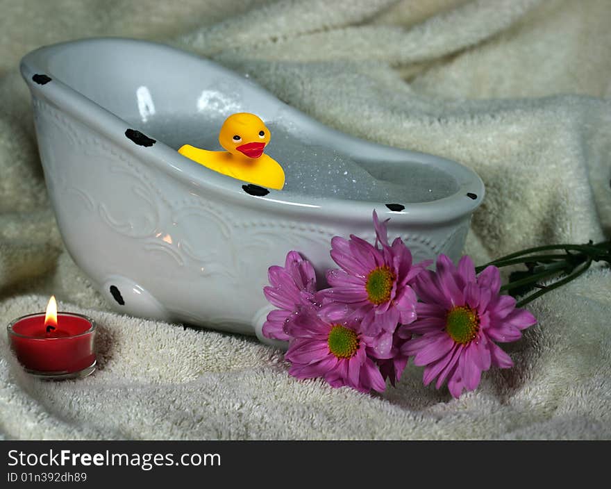 Little duckie taking a bubble bath with flowers and candle on a towel. Little duckie taking a bubble bath with flowers and candle on a towel