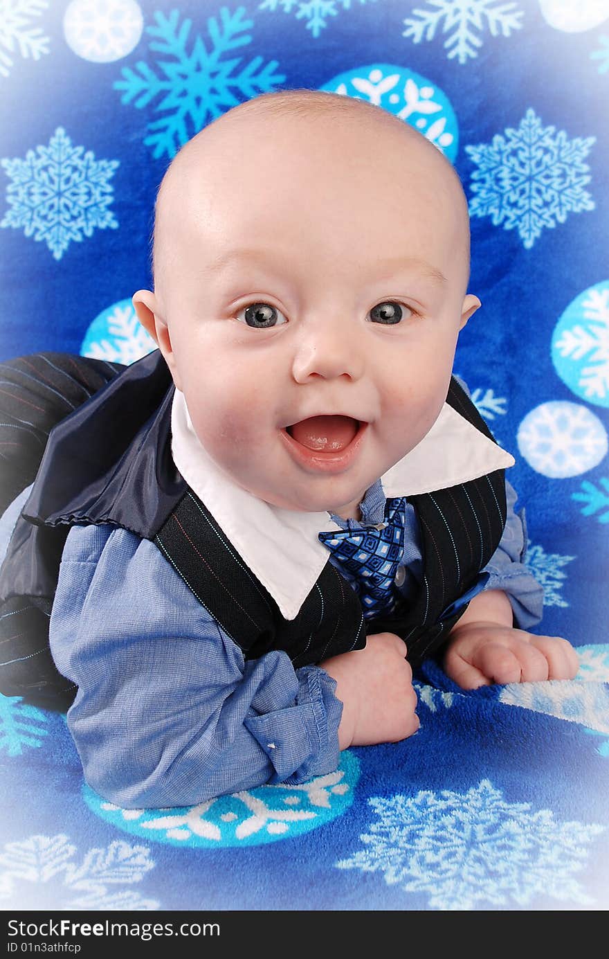 Blue eyed 5 month old smiling towards the camera. He is dressed in a suit type outfit. The photo was taken on a blue blanket with snowflakes. Blue eyed 5 month old smiling towards the camera. He is dressed in a suit type outfit. The photo was taken on a blue blanket with snowflakes.