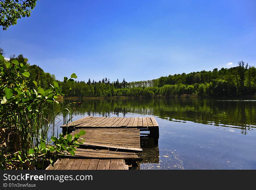 Landscape with lake, forest, footbridge.