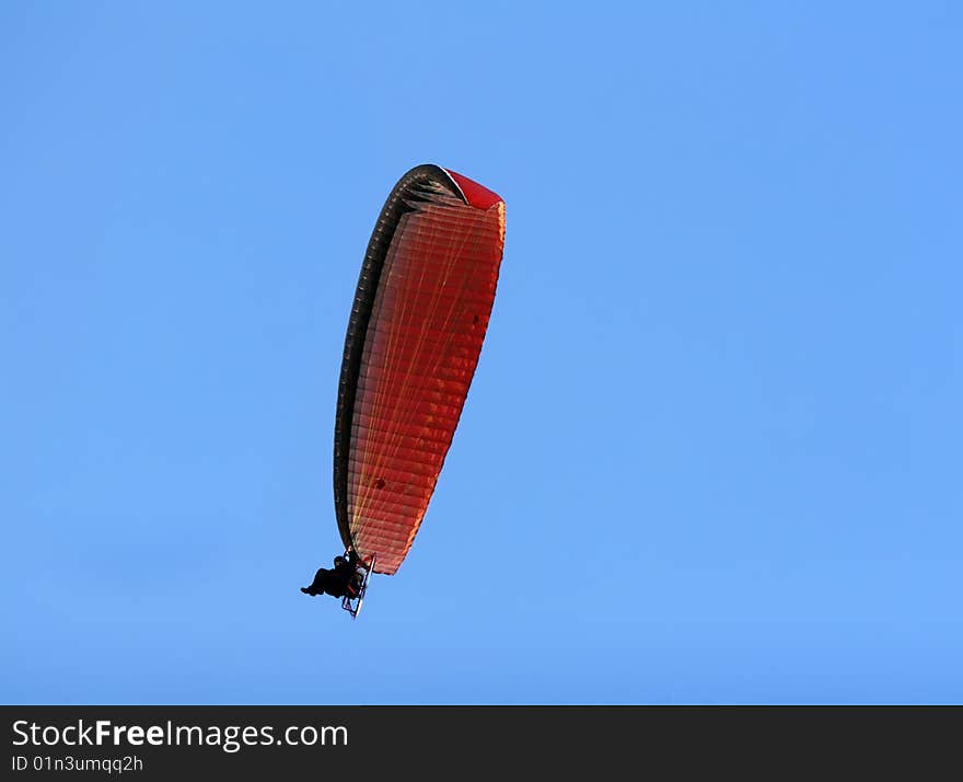 A paramotor flying high above in the blue sky. A paramotor flying high above in the blue sky