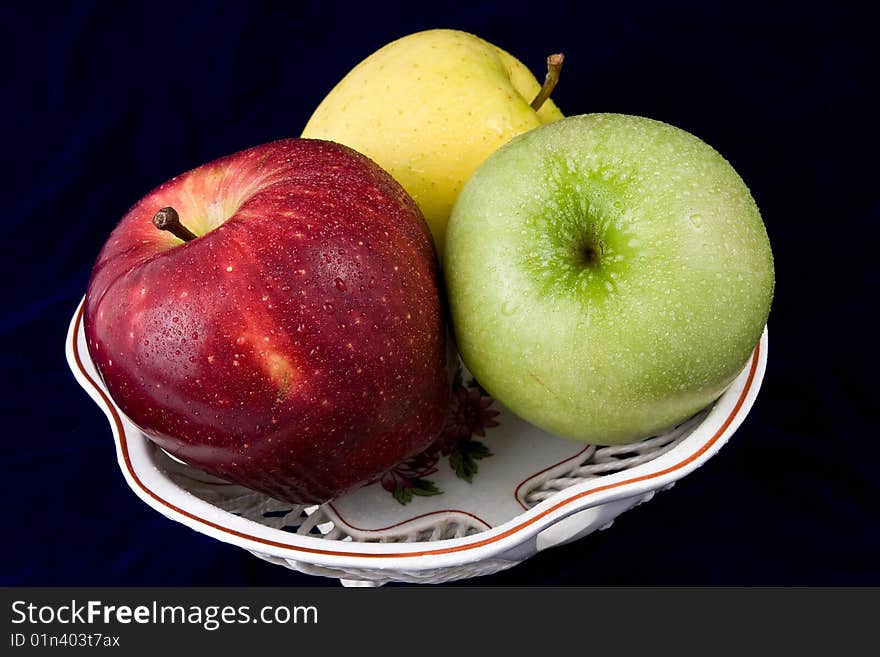 Three apples in a vase, are photographed on a dark blue background