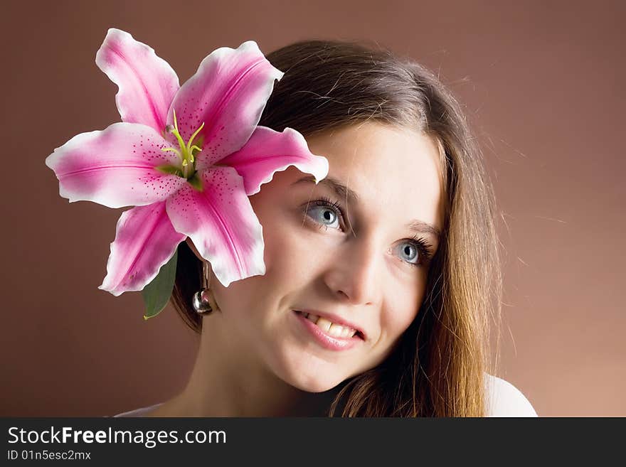 A pretty young woman with long brown hair posing with a pink lily near her face. A pretty young woman with long brown hair posing with a pink lily near her face