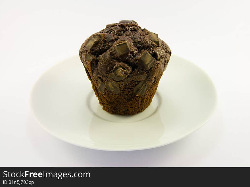 Single chocolate muffin on a white plate with a white background. Single chocolate muffin on a white plate with a white background