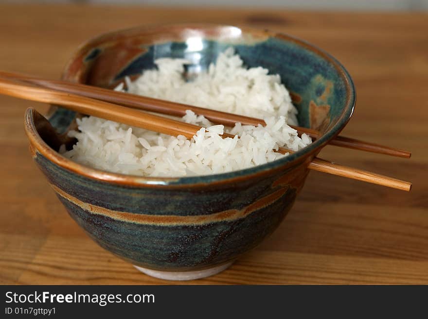 A bowl of steamed rice with wooden chopsticks through holes of the bowl on a wooden surface. A bowl of steamed rice with wooden chopsticks through holes of the bowl on a wooden surface.