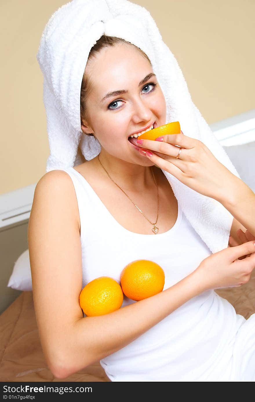 Pretty young woman sitting on the bed at home and eating oranges. Pretty young woman sitting on the bed at home and eating oranges