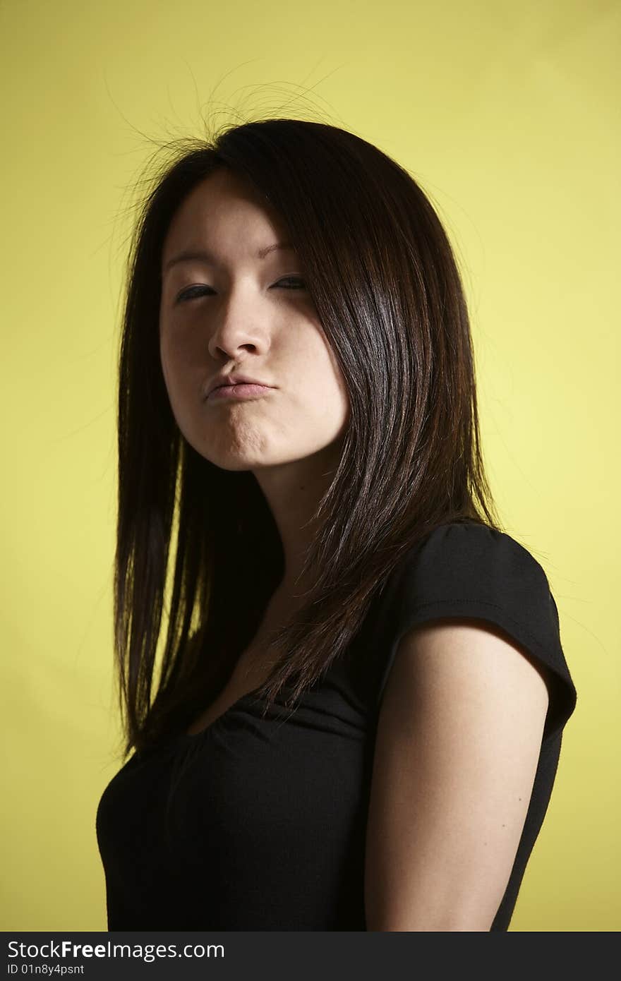 Young Asian woman wearing a black top against a yellow background makes a pouting expression at the camera. Young Asian woman wearing a black top against a yellow background makes a pouting expression at the camera.