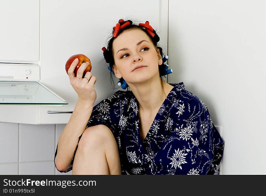 Young woman sitting in the kitchen and eating an apple. Young woman sitting in the kitchen and eating an apple