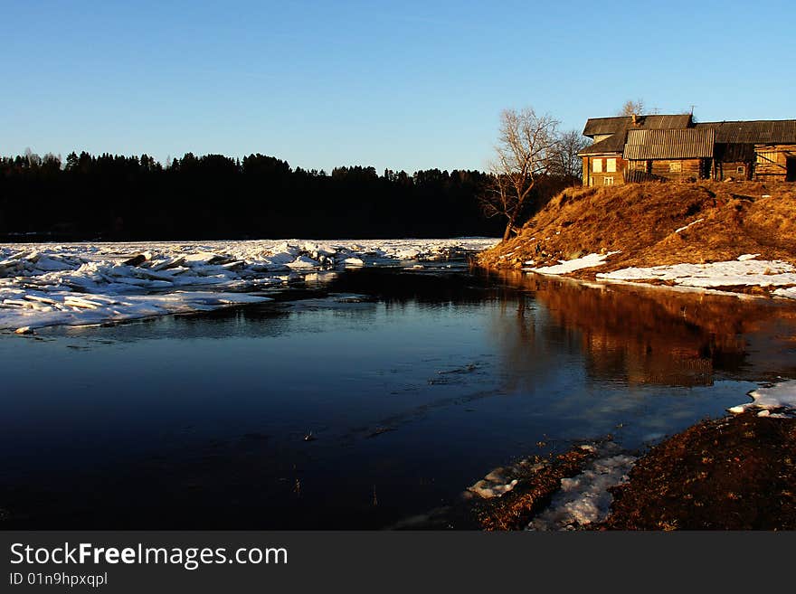 An old shed next to a snowy river bank in the mountains.